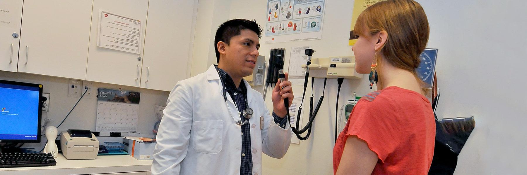 澳门新葡新京官方的工作人员穿着白大褂，拿着听诊器检查坐在医疗台上的学生